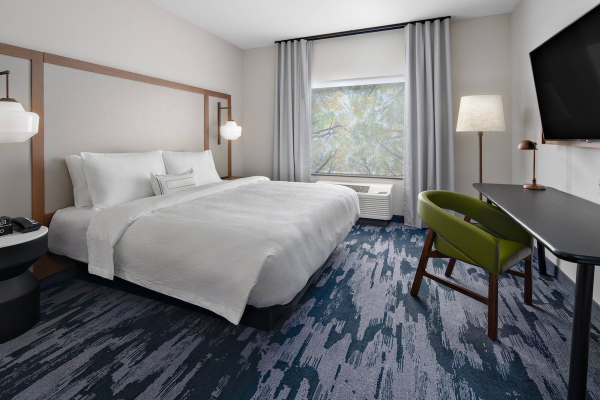 A hotel room with a large bed, a desk, a chair, a TV, and a window with curtains.