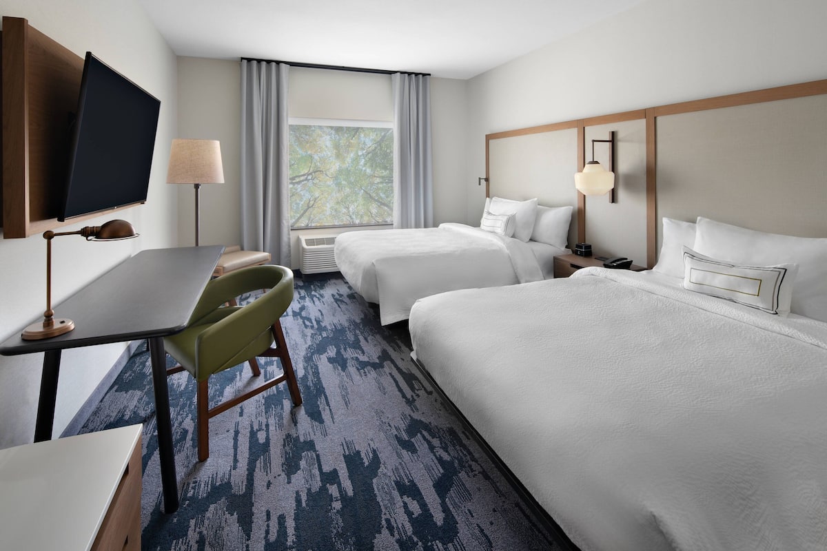 A hotel room with two beds, a desk, a chair, a TV, and a window with curtains.