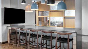 A modern kitchen with a bar area, pendant lights, and a flat-screen TV.