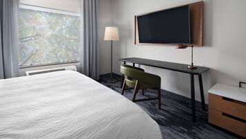 A hotel room with a large bed, a desk with a chair, a television, and a window with curtains.