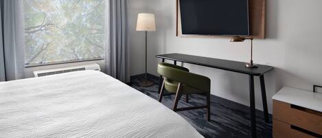 A hotel room with a large bed, a desk with a chair, a television, and a window with curtains.