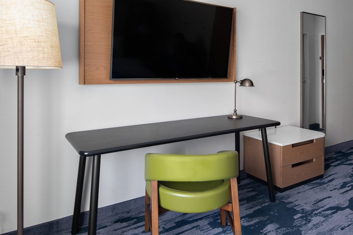 A room with a desk, a chair, a lamp, a mirror, and a television.