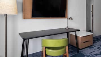 A room with a desk, a chair, a lamp, a mirror, and a television.