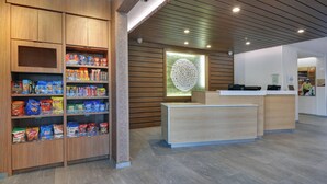 Ein moderner Empfangsbereich mit Holzregalen voller Snacks, einem hellen Empfangstresen und einem dekorativen Wandkunstwerk.