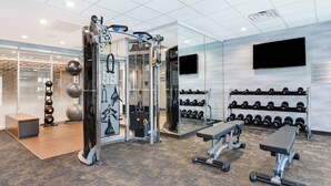 Ein Fitnessraum mit Trainingsgeräten, einer Bank und einem an der Wand befestigten Fernseher.