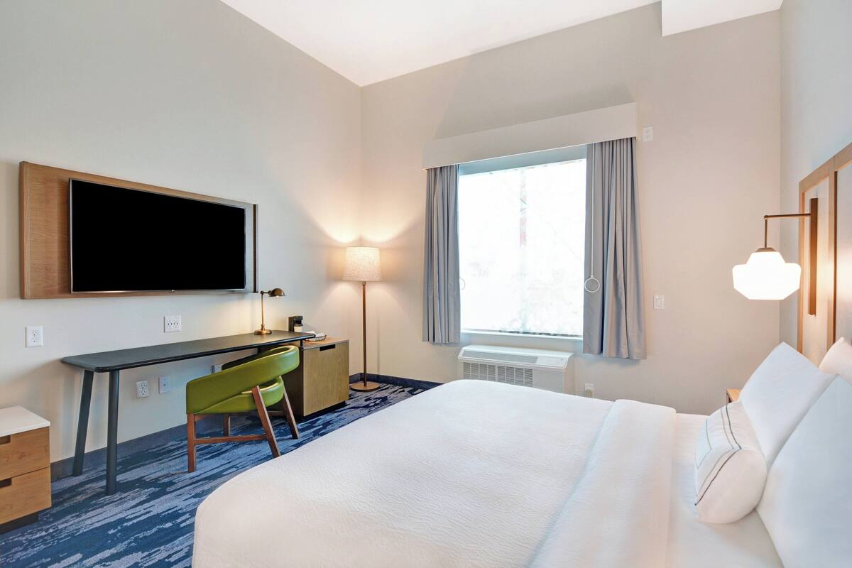 Une chambre d’hôtel équipée d’un lit, d’un bureau, d’une chaise, d’une télévision, d’une lampe, d’une fenêtre et d’un appareil de climatisation.