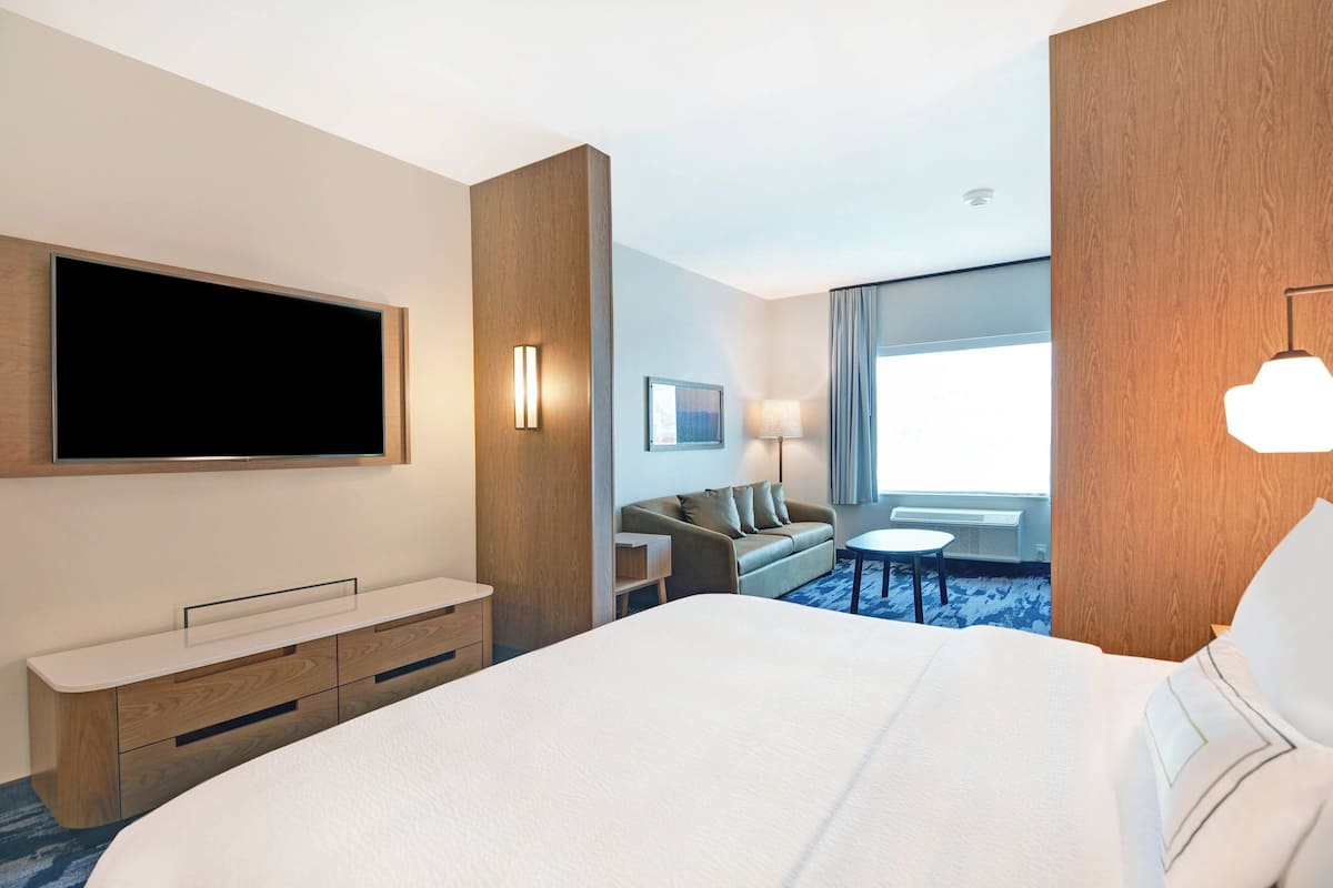 Une chambre d’hôtel avec un grand lit, un téléviseur à écran plat, une commode en bois, un canapé, une petite table et une fenêtre avec des rideaux.
