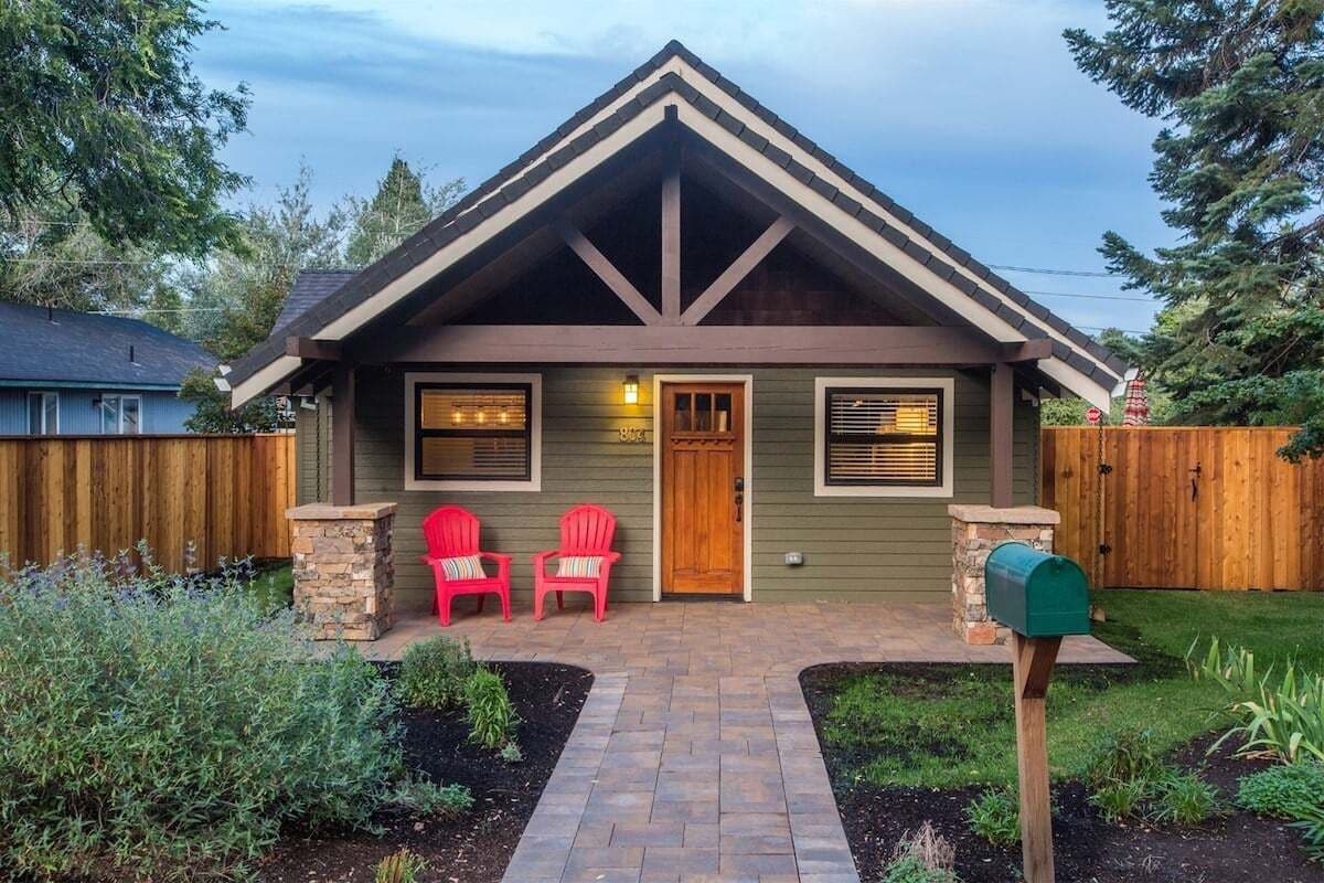 A two-story house with a gabled roof, a front porch with two red chairs, and a mailbox.