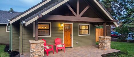 A house with a gabled roof, a front porch with two red Adirondack chairs, and a stone pillar.