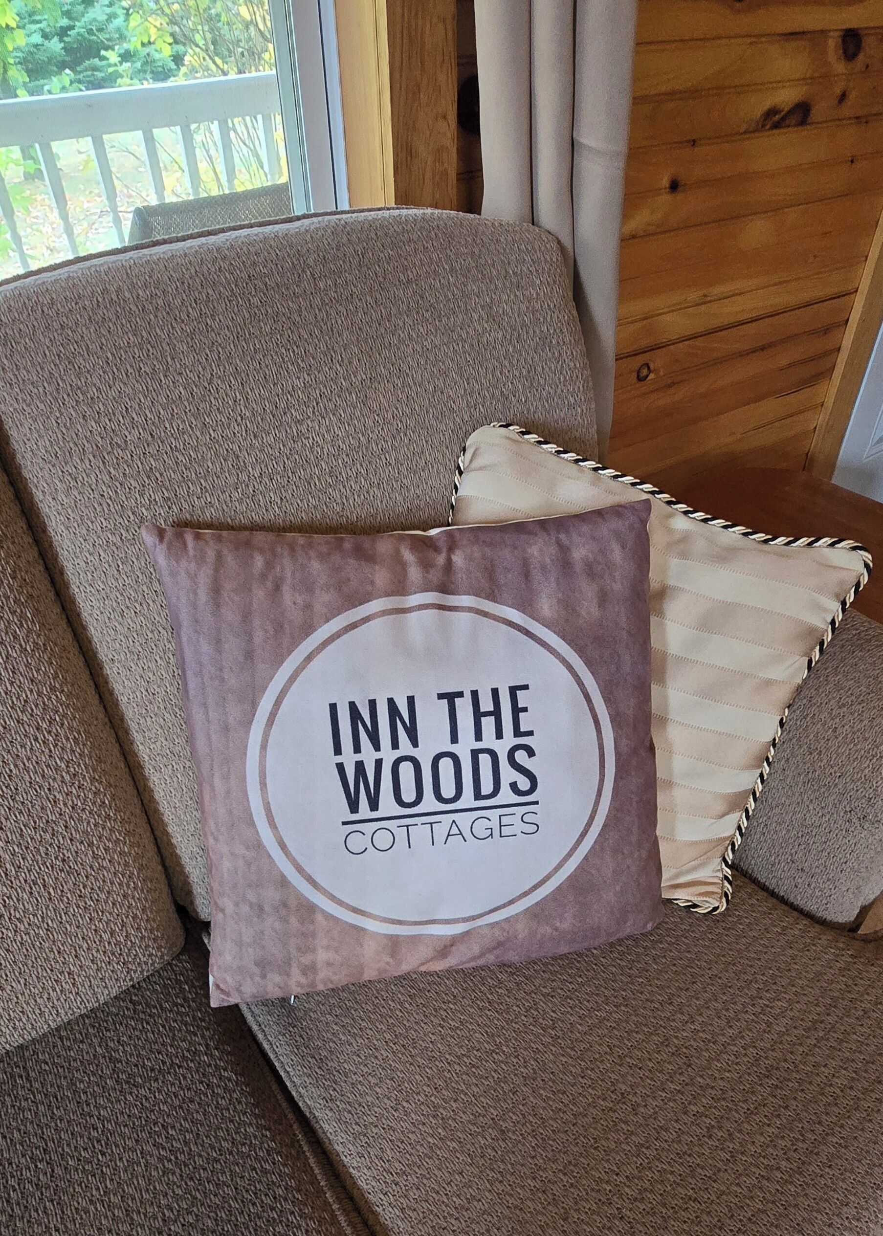 Beigenvärinen sohva, jossa on pyöreä logolla varustettu koristetyyny. Logossa lukee: ”INN THE WOODS COTTAGES”.