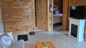 A cozy cabin-style room with a wooden interior, a sofa, a coffee table, a fireplace, and a television.