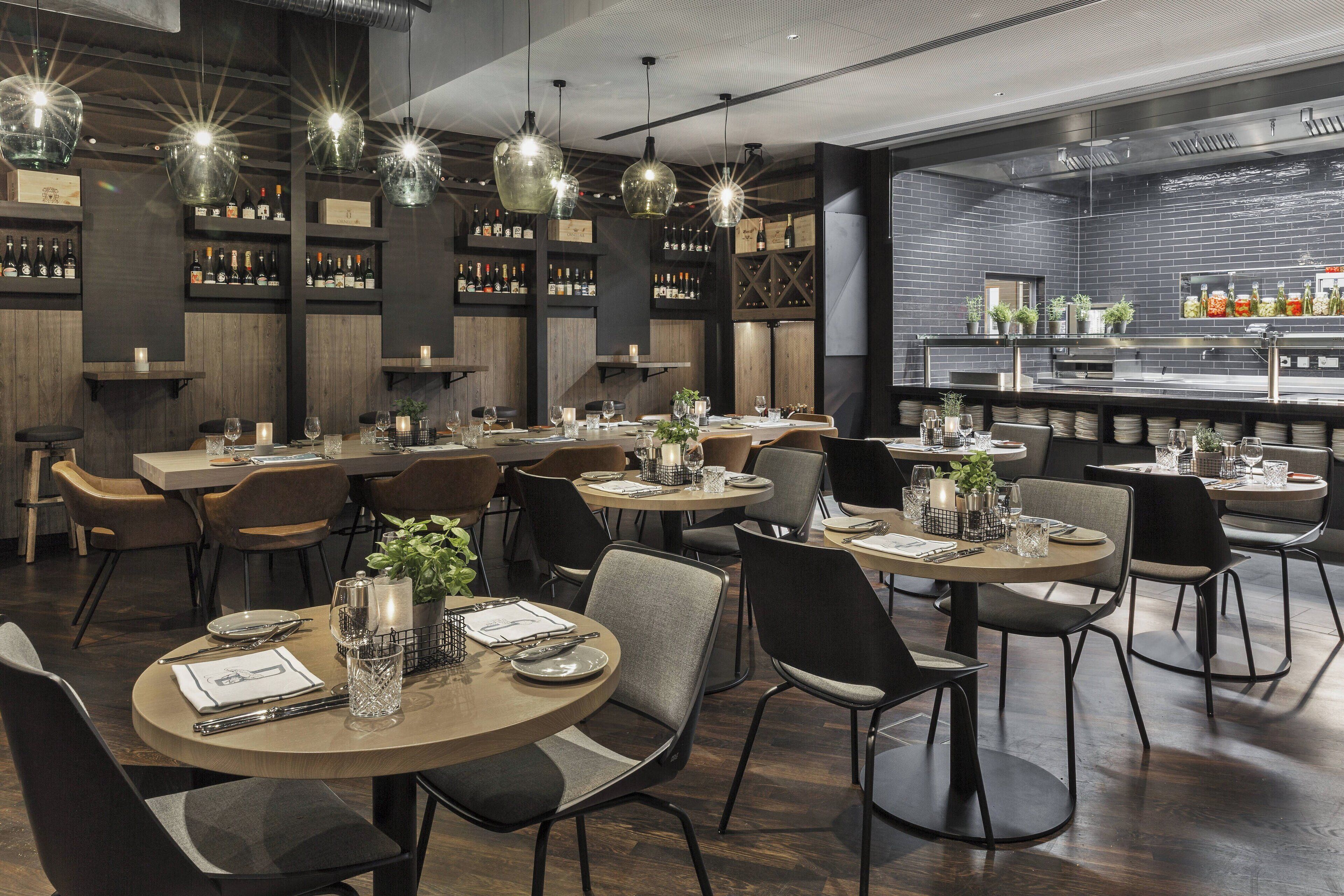 Un interno ristorante moderno con tavoli rotondi, sedie nere e lampade a sospensione.