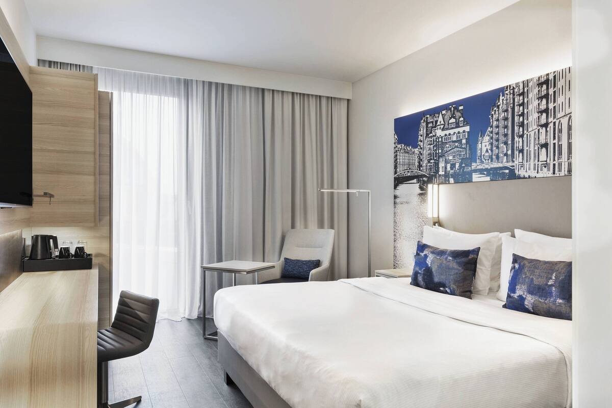Habitación de hotel con una cama grande, un escritorio, una silla y un cuadro en la pared.
