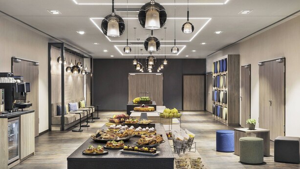 Un hall d’hôtel moderne doté d’un long comptoir d’accueil, d’un espace salon et d’une variété de choix en matière de nourriture et de boissons.