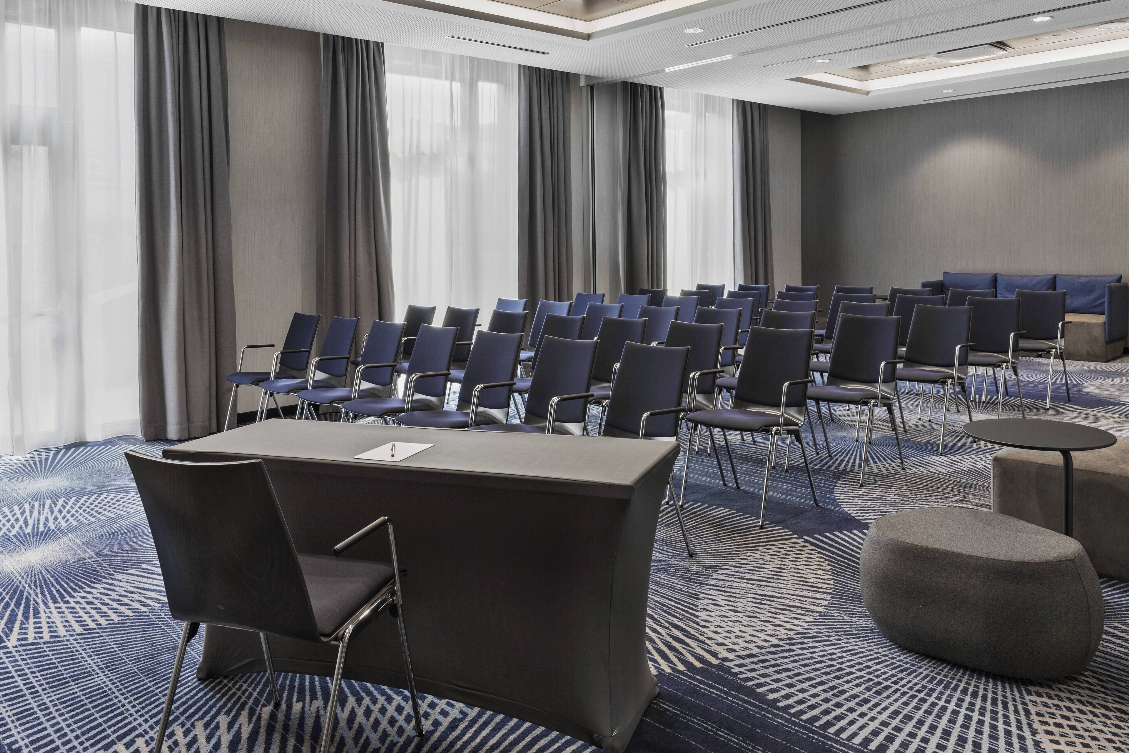 Une salle de conférence avec des rangées de chaises, une table et un sol recouvert de moquette.