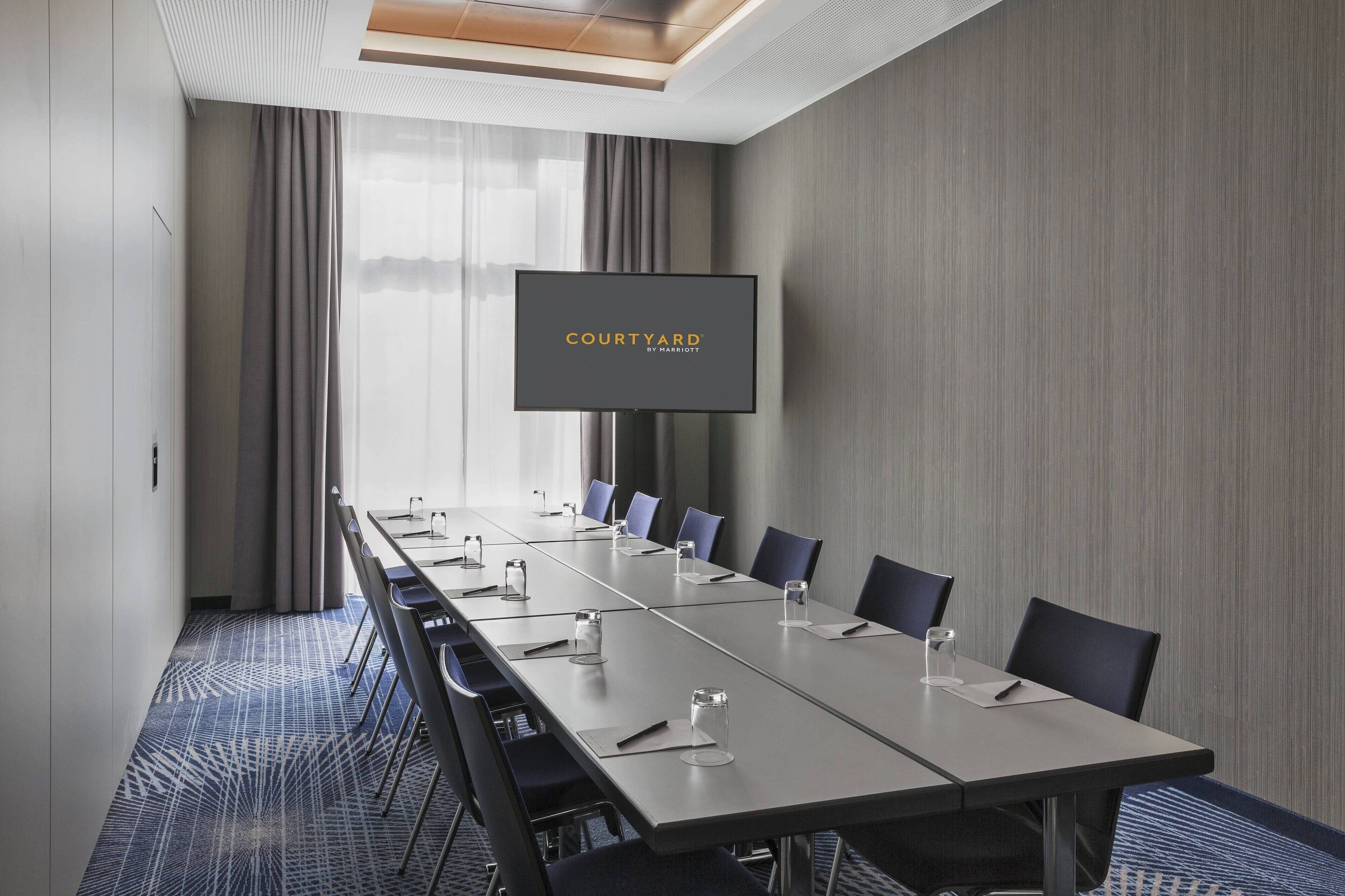 A conference room with a long table, chairs, a flat-screen TV, and a view of the outdoors.
