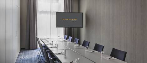 Un salón de conferencias con una larga mesa, sillas, un televisor de pantalla plana y vistas al exterior.