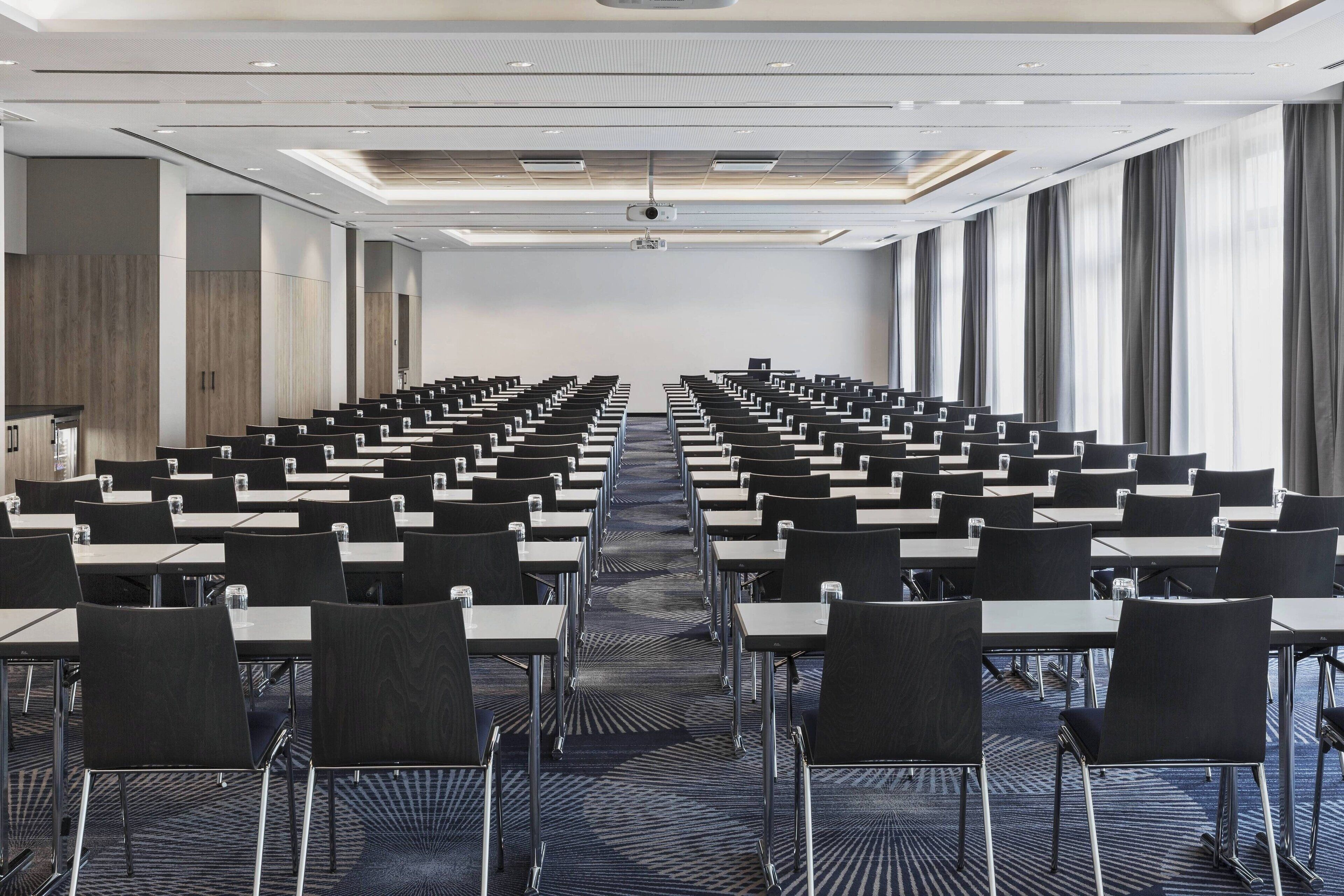 A conference room with rows of tables and chairs, a projector, and large windows.