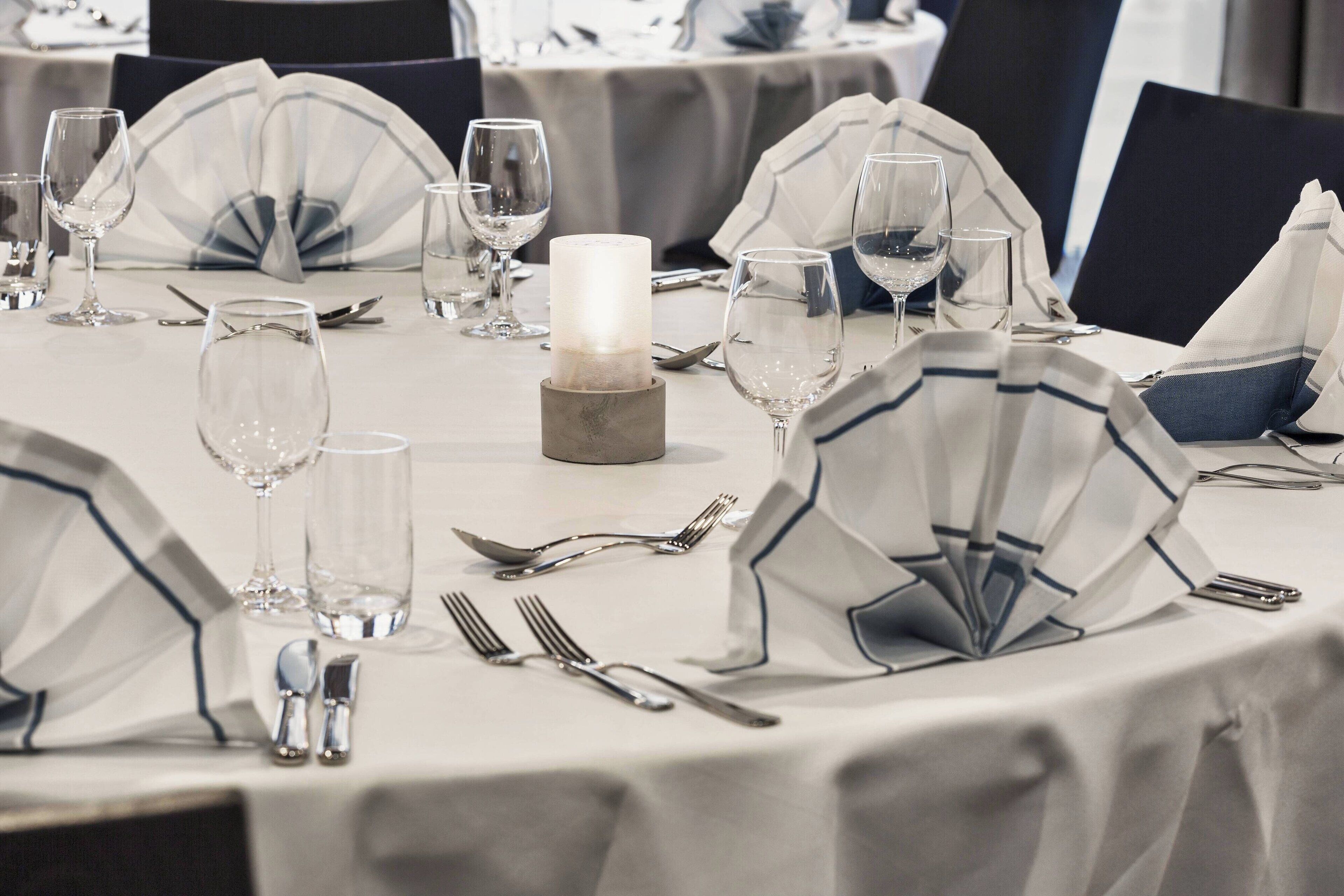 A table set for dining with clear glassware, a candle centerpiece, and a white tablecloth.