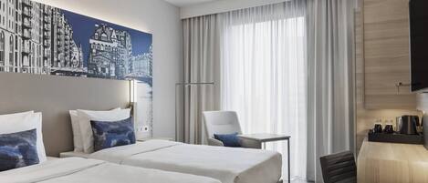 A hotel room with two beds, a desk, a chair, a TV, and a large window with curtains.