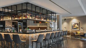 Un espace bar moderne doté d’un comptoir haut, de nombreux tabourets et d’une grande variété de bouteilles et de verres.
