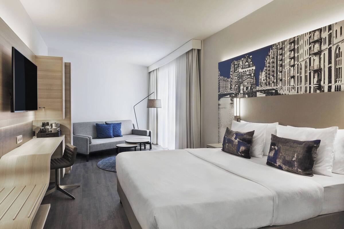 Una habitación de hotel moderna con una cama grande, un sofá, un escritorio y un televisor de pantalla plana.