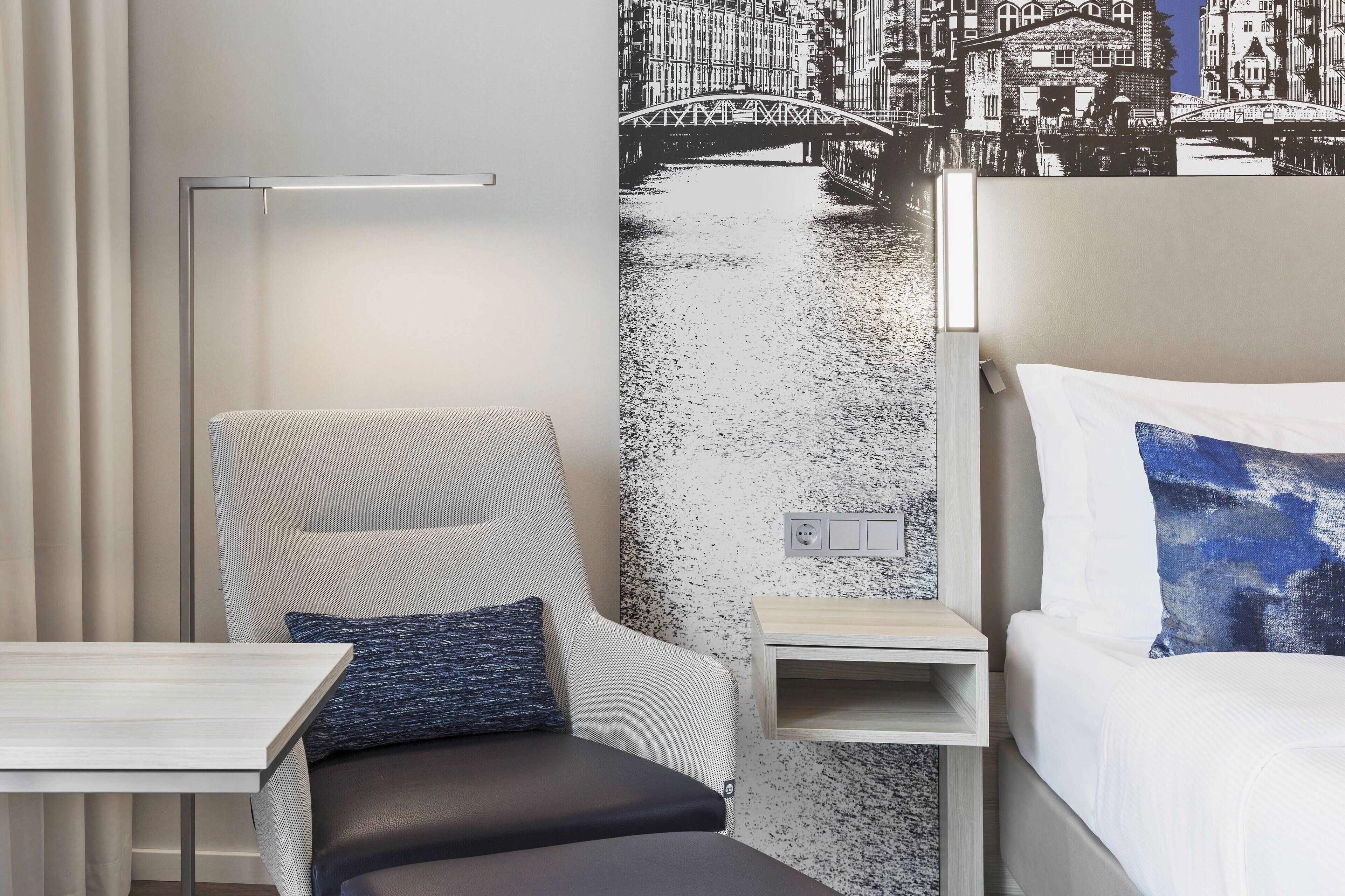 Une chambre d’hôtel avec un lit, une chaise, une petite table et une fresque murale représentant un pont au-dessus de l’eau.