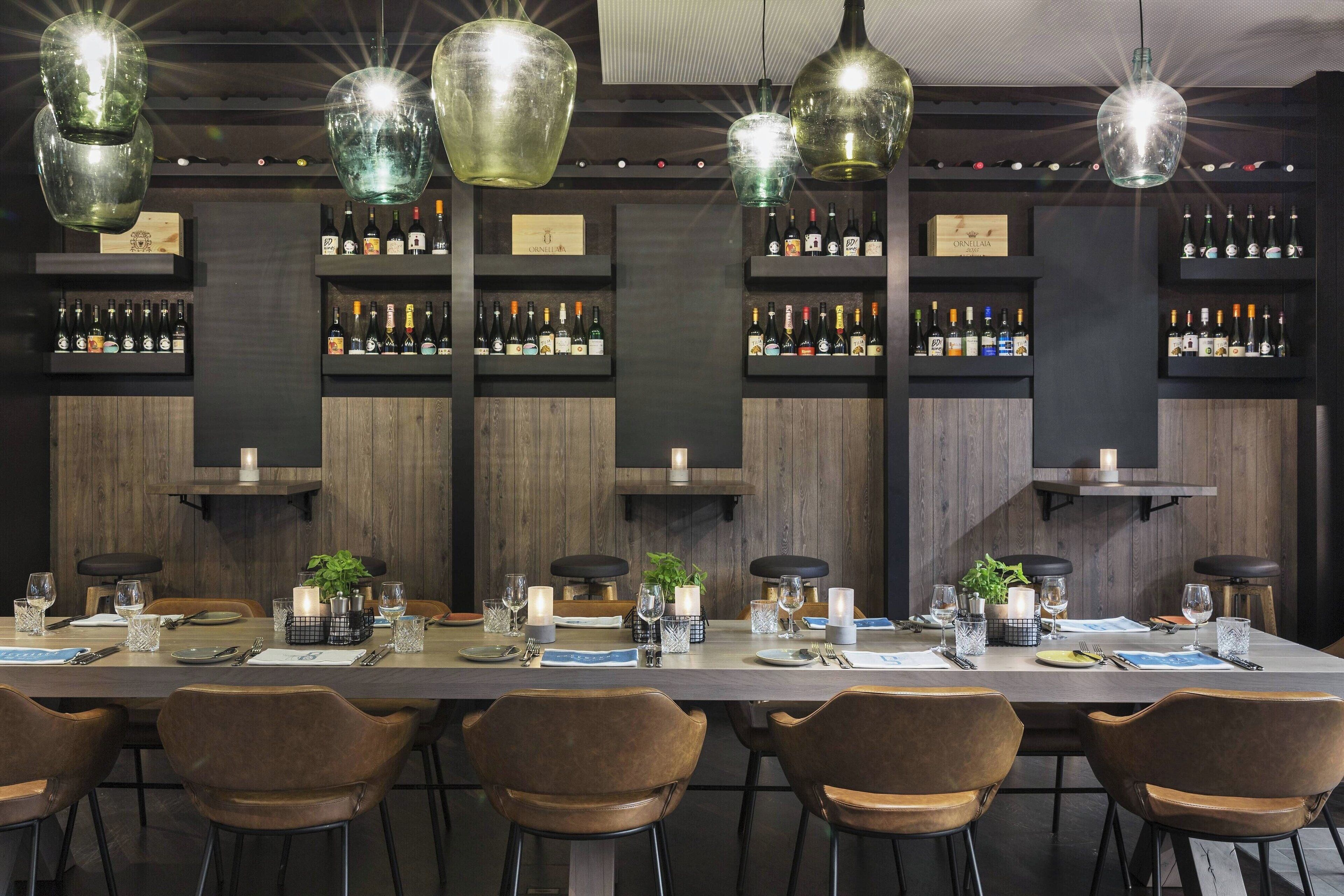A bar area with multiple shelves of liquor bottles, hanging glass pendant lights, and a long dining table set for six with chairs.