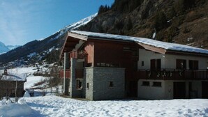 Ein Chalet mit Steinunterbau und Holzkonstruktion, vor einer verschneiten Bergkulisse.