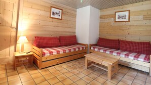 Ein gemütliches Zimmer mit Holzwänden, einer Sofaecke, einem kleinen Tisch und einer Lampe.