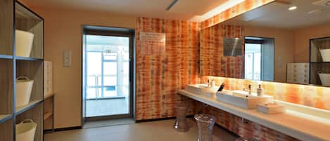 A modern bathroom with two sinks, a large mirror, and a wooden shelf with baskets.
