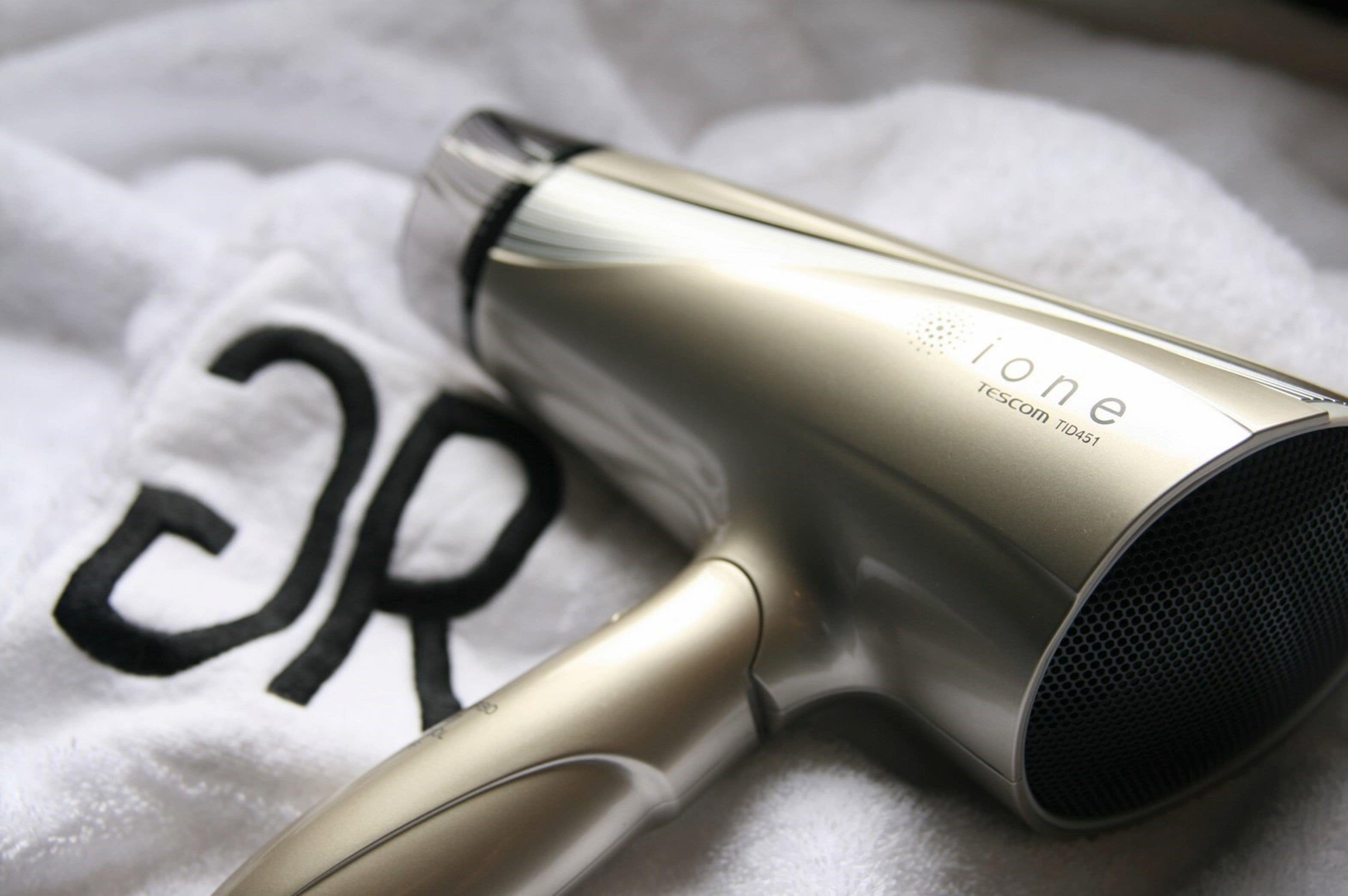 A gold-colored hair dryer with the brand name 'ione' and model number 'TESCOM TID151' on a white fabric background.