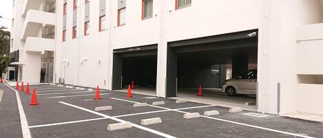 A parking area with marked spaces and orange traffic cones, leading to a building with multiple floors and balconies.