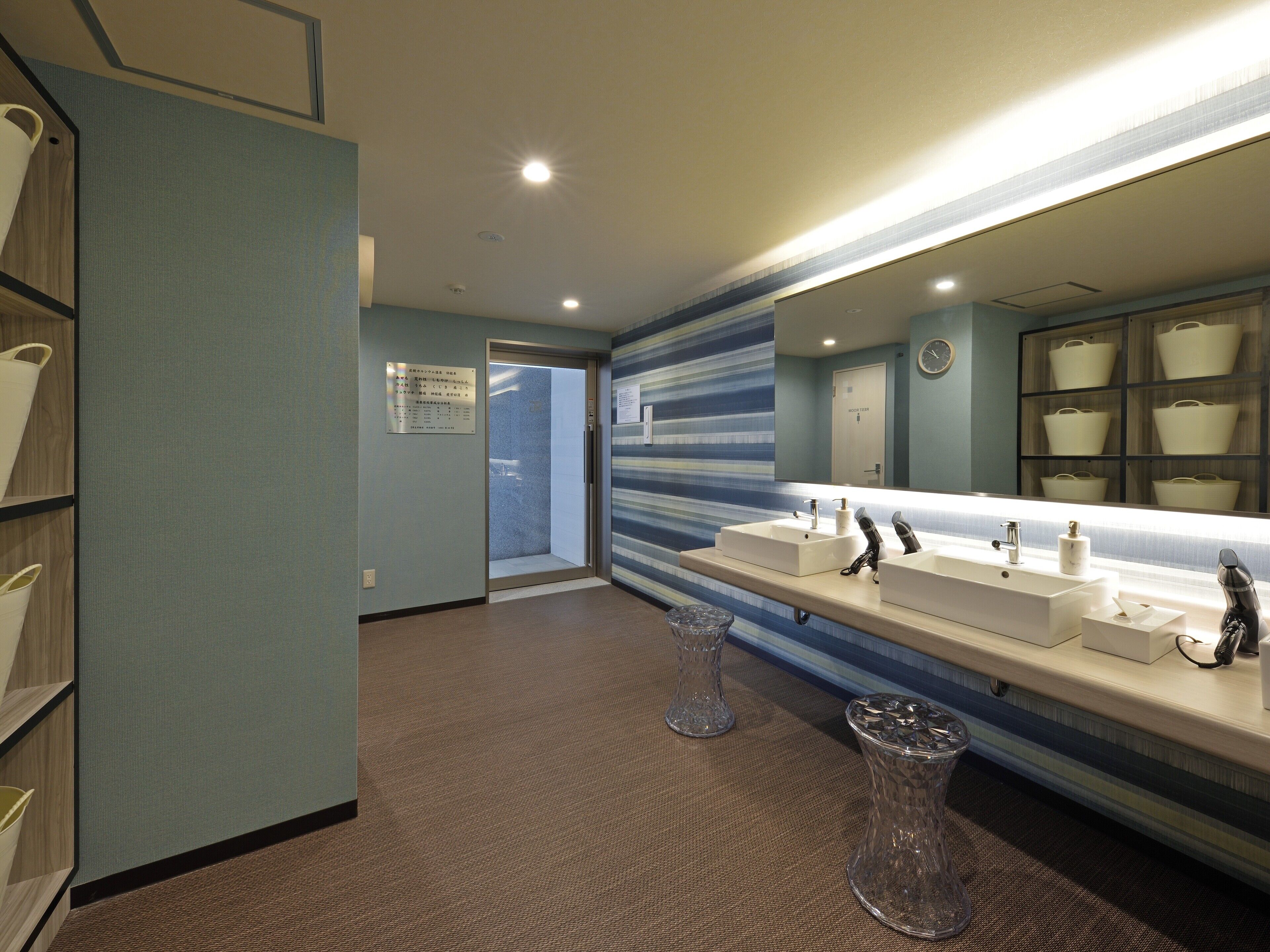A modern bathroom with a large mirror, two sinks, and a storage unit with baskets.
