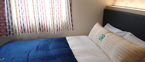 Una cama con una manta azul y almohadas a rayas, un cabecero y una ventana con cortinas.