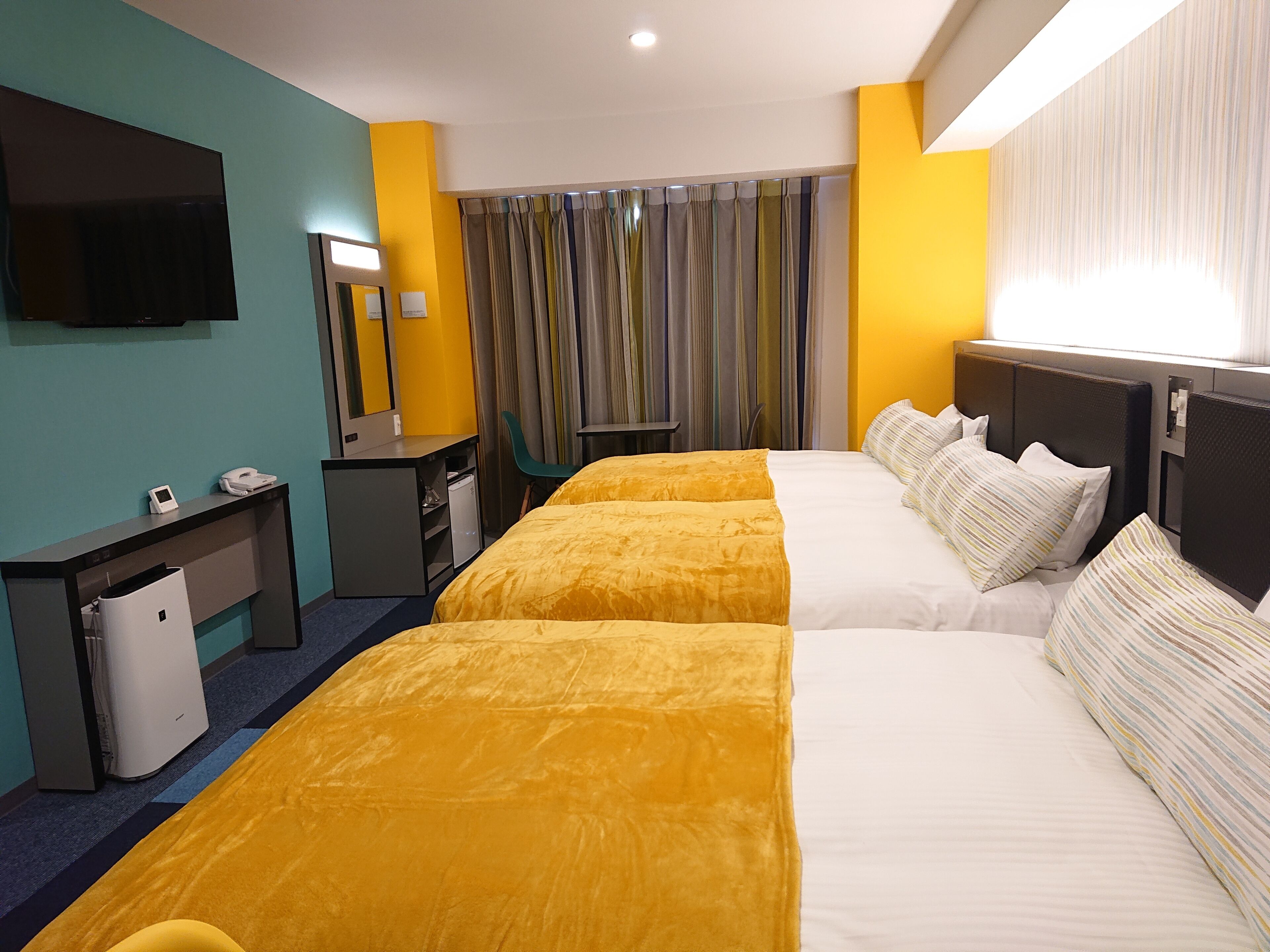 A hotel room with two beds, a desk with a phone, a small fridge, and a TV mounted on the wall.