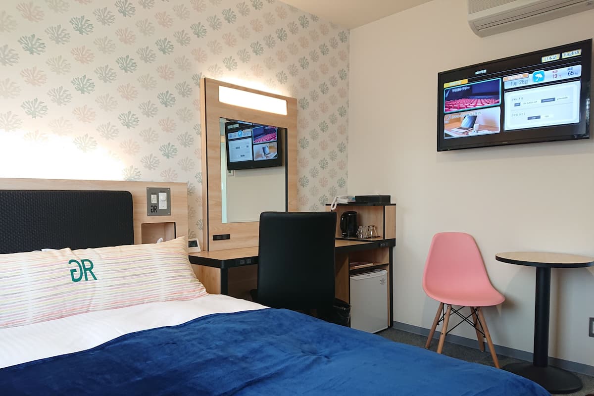 Une chambre d’hôtel équipée d’un lit, d’un bureau, d’une chaise, d’une petite table et d’un téléviseur fixé au mur.