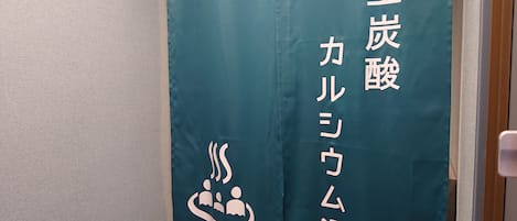 Cortina azul-turquesa com texto em japonês e um logotipo com três figuras e a palavra 'MEN'.