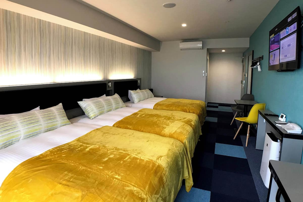 Une chambre d’hôtel avec deux lits, un bureau, une chaise et un téléviseur fixé au mur.