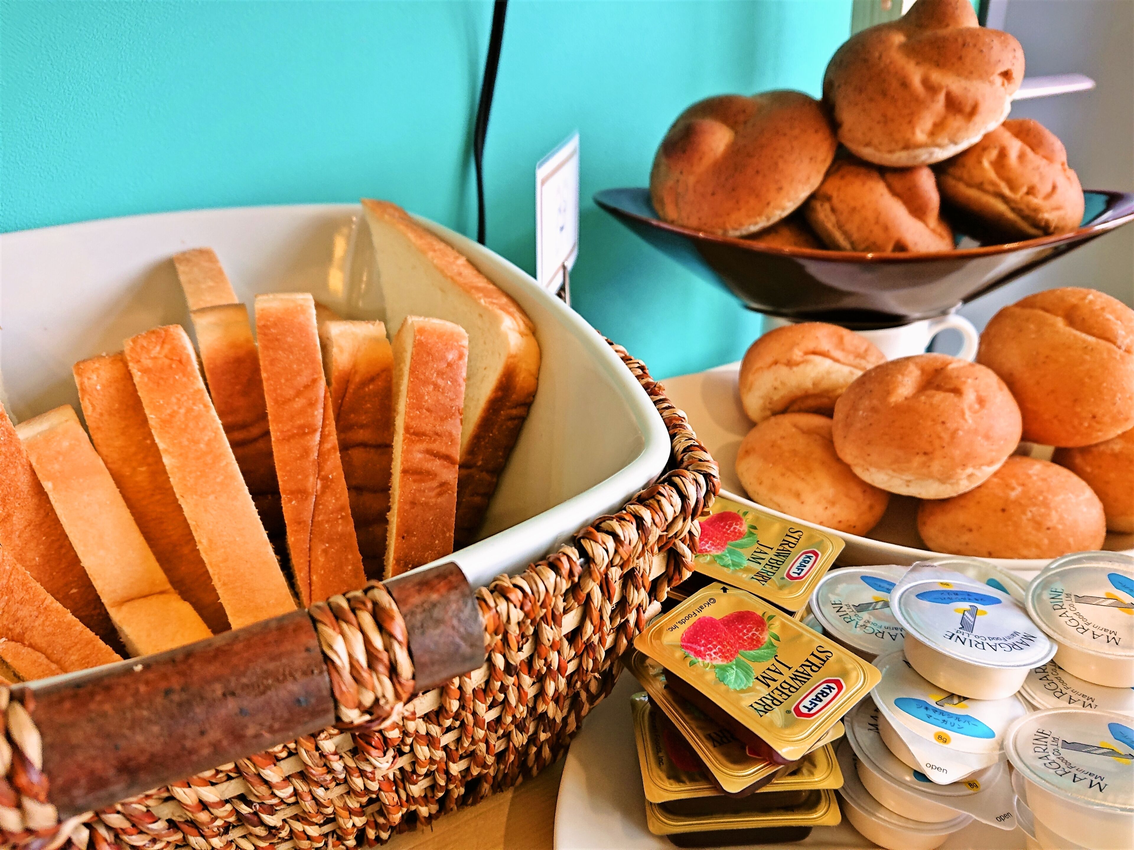 Une table de buffet avec du pain tranché, des petits pains et des pots de confiture de fraises.