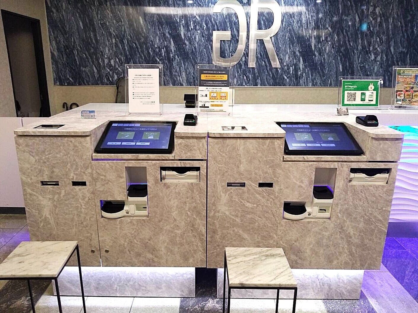 A reception desk with two digital kiosks, a marble counter, and a sign with QR codes.