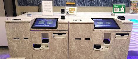 A reception desk with two digital kiosks, a marble counter, and a sign with QR codes.