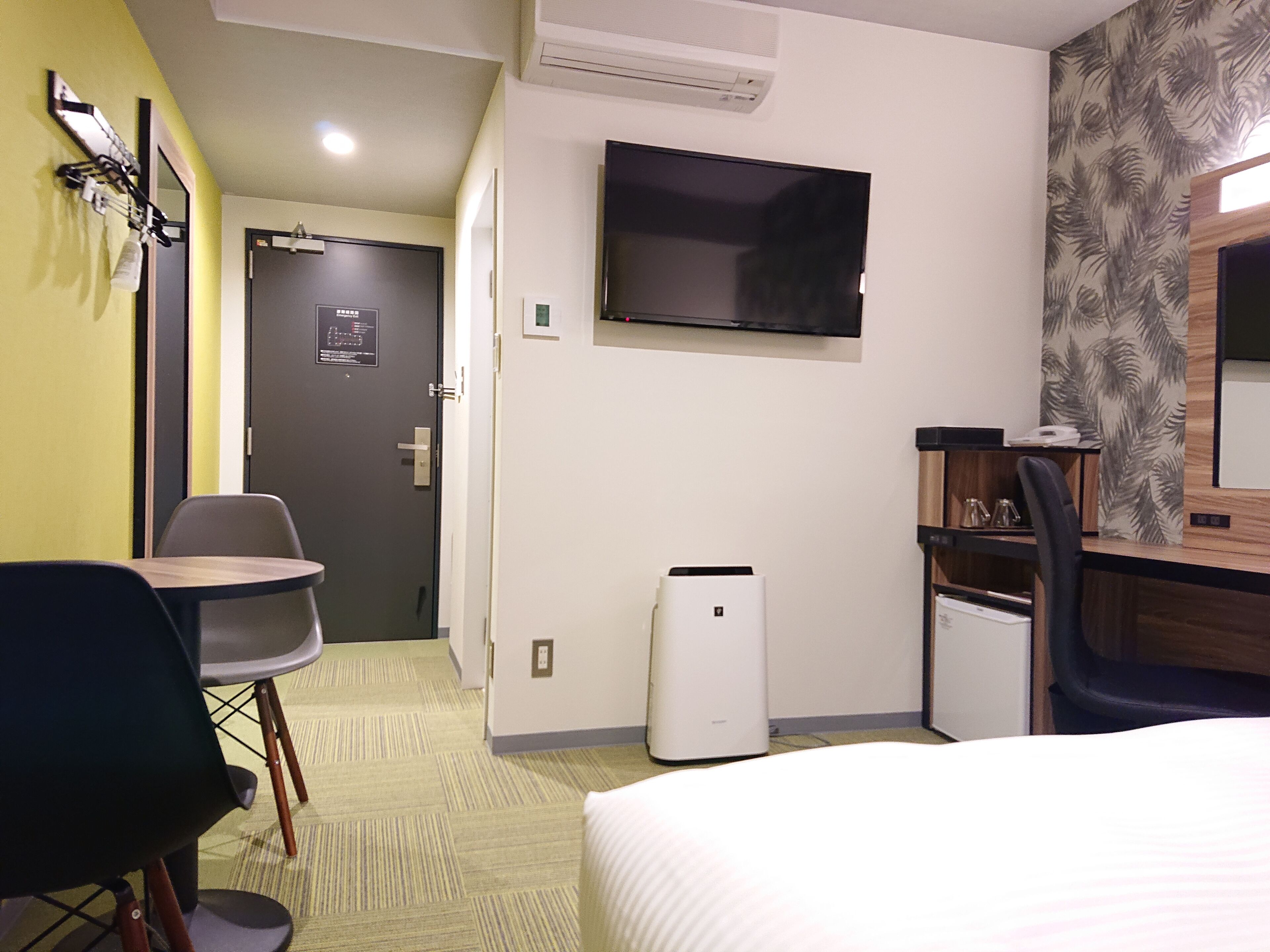 Une chambre d’hôtel comprenant un lit, un bureau avec une chaise, un téléviseur fixé au mur et un appareil de climatisation.