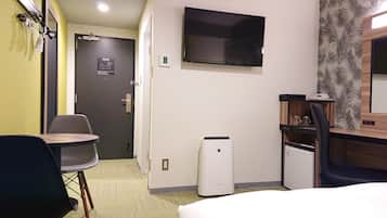 Habitación de hotel con cama, escritorio con silla, televisor montado en la pared y equipo de aire acondicionado.