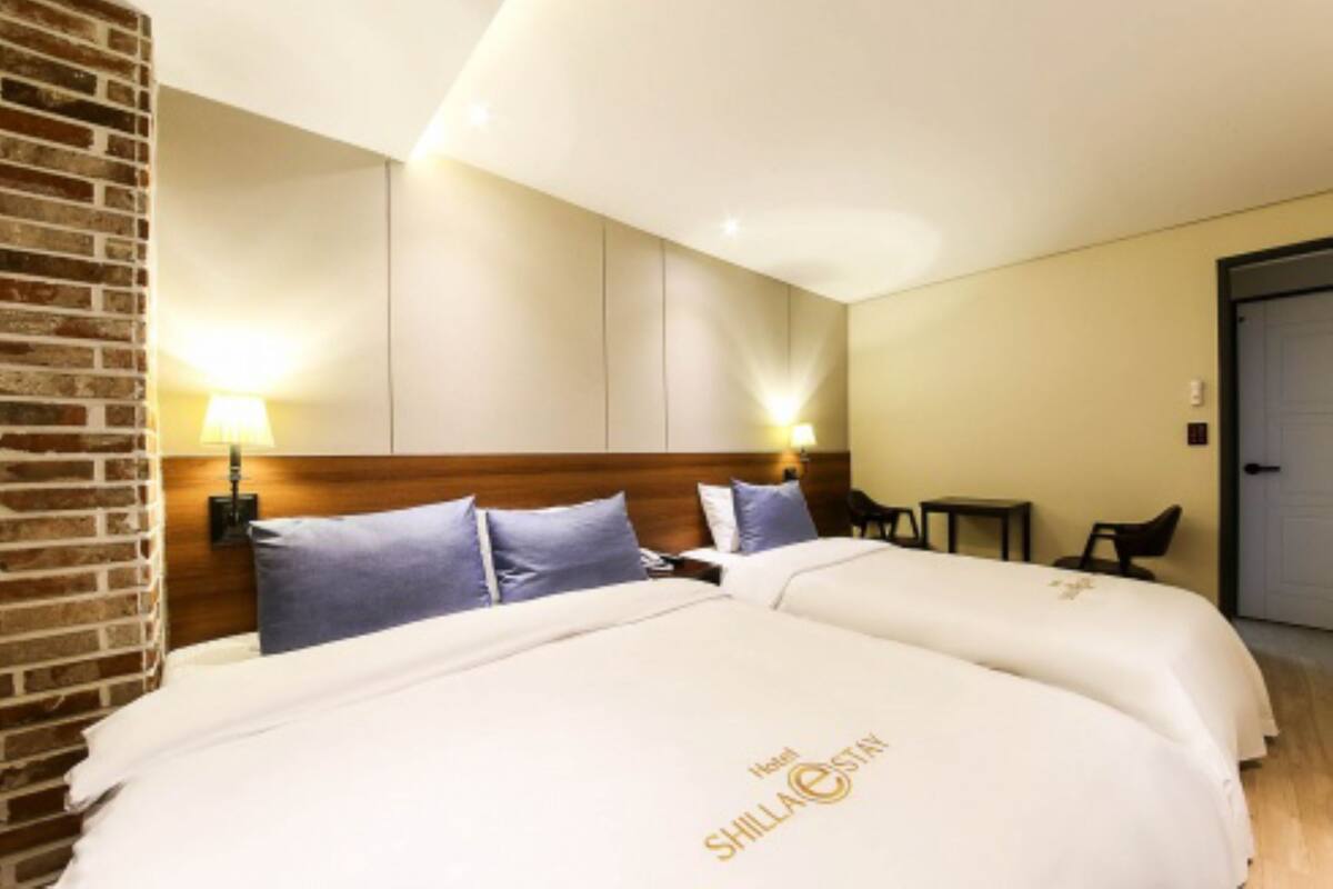 A hotel room with a large bed, two bedside tables, a wooden headboard, and a brick accent wall.