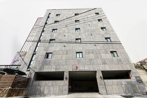 A multi-story building with a parking garage entrance, a sign for 'SHILLA stay', and a 'PARKING' sign above the garage. - Shilla E Stay Motel (Yeosu)