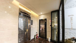A hotel lobby with a modern design, featuring a marble wall, a glass elevator, and a brick wall with the hotel name. - Shilla E Stay Motel (Yeosu)