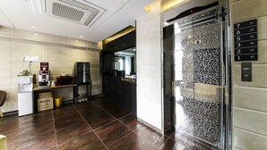 A hotel lobby with a reception desk, a coffee machine, a refrigerator, and a glass elevator. - Shilla E Stay Motel (Yeosu)