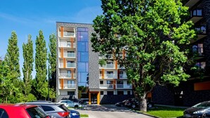 Un edificio residencial de varios pisos con balcones, un estacionamiento y un árbol en primer plano.