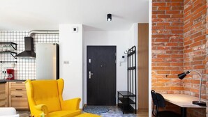 Un espacio habitable moderno con un sillón amarillo, una mesita, un escritorio con una silla, una puerta negra y una pared de ladrillo.
